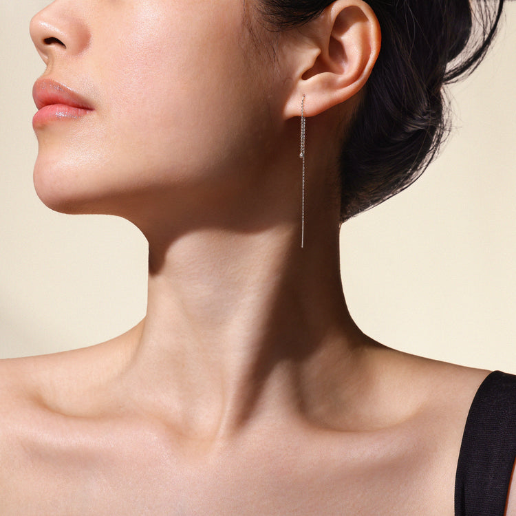Close-up of a woman's ear wearing a white gold dangling earring with a neutral background.