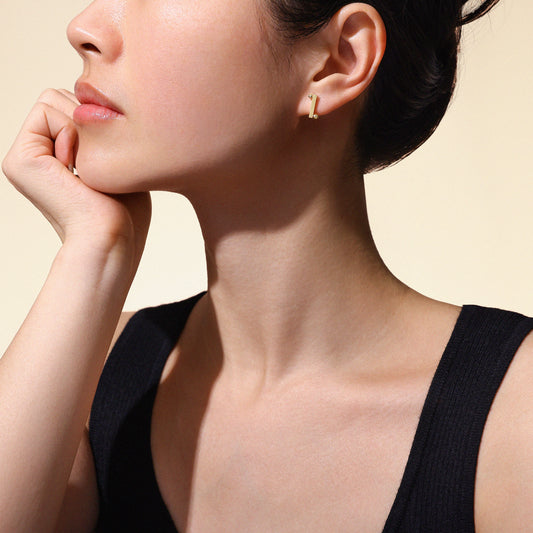 Woman wearing gold stud earrings made from 18k yellow gold on a neutral background
