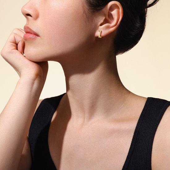 Woman wearing gold stud earrings made from 18k yellow gold on a neutral background