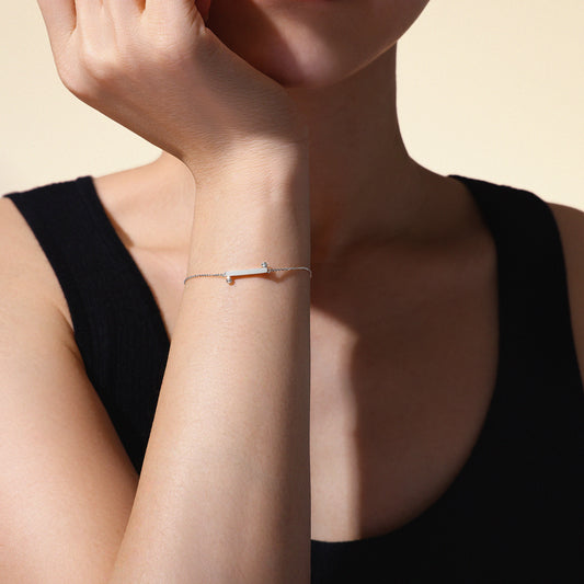 Woman's arm wearing a thin 18k white gold bracelet on a neutral background