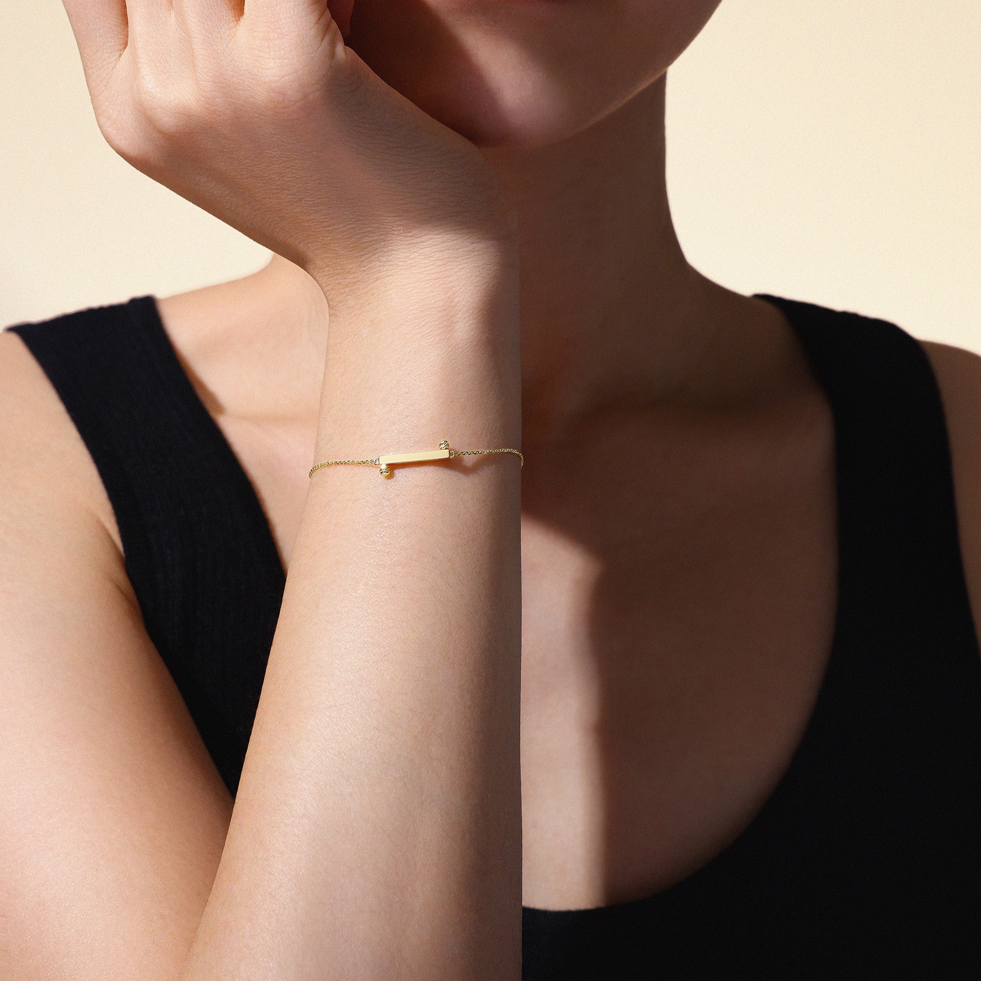 Woman's arm wearing a thin 18k yellow gold bracelet on a neutral background