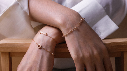 Close-up of a person's wrist and hand wearing multiple rose gold bracelets on a wooden surface.