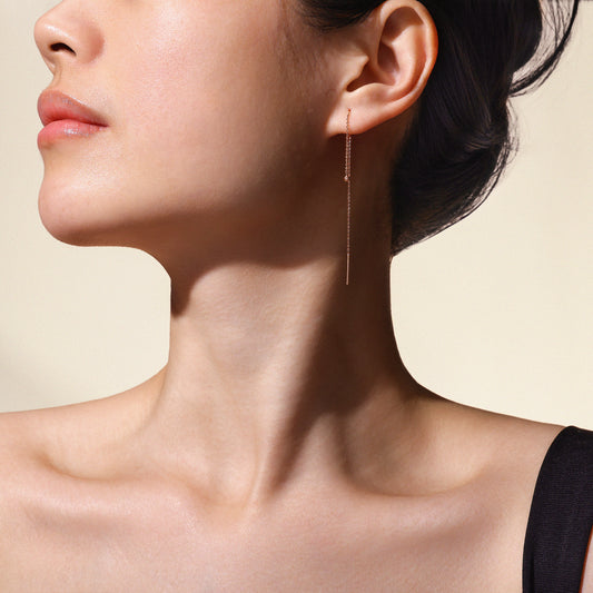 Close-up of a woman's ear with a dangling earring against a neutral background.