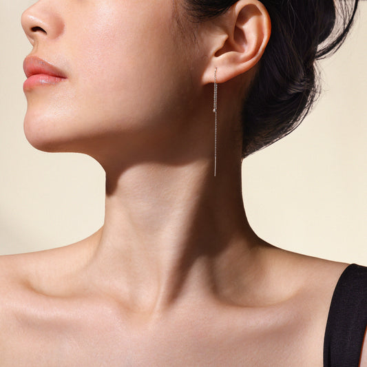 Close-up of a woman's ear wearing a white gold dangling earring with a neutral background.