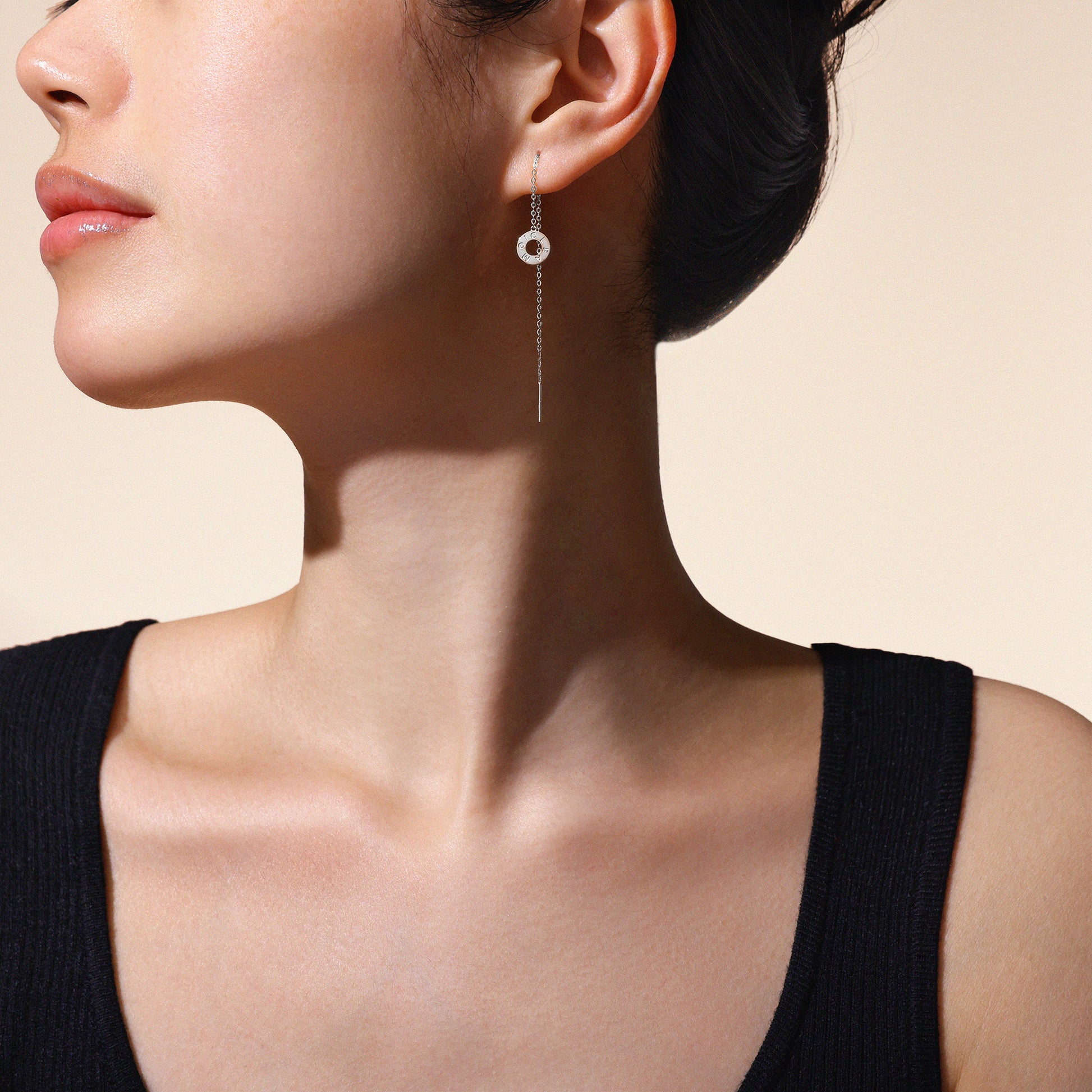 A model wearing Just Cléamoi earrings, which are 18k white gold with a small circle design on a chain.