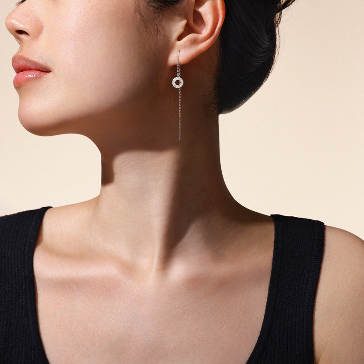 A model wearing Just Cléamoi earrings, which are 18k white gold with a small circle design on a chain.