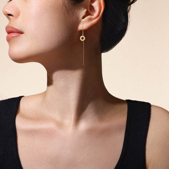 A model wearing Just Cléamoi earrings, which are 18k yellow gold with a small circle design on a chain.