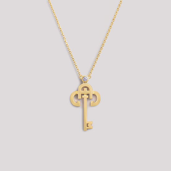 A yellow gold necklace with a key-shaped pendant, featuring a diamond at the top of the key.