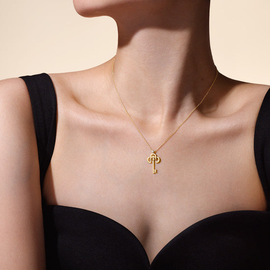 A gold-colored necklace with a key-shaped pendant, worn by a model.